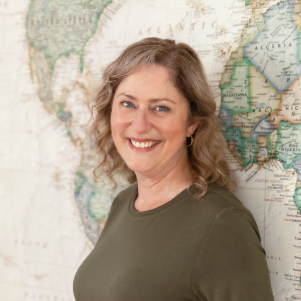 Headshot of a smiling Marketing Coordinator for Icon Adventures, standing confidently in front of a world map. Laurene is looking directly at the camera, conveying professionalism and warmth.